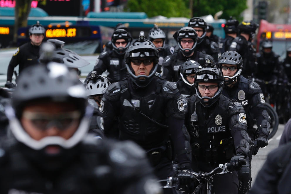 A large group of helmeted bicycle officers sit tightly grouped on their bikes