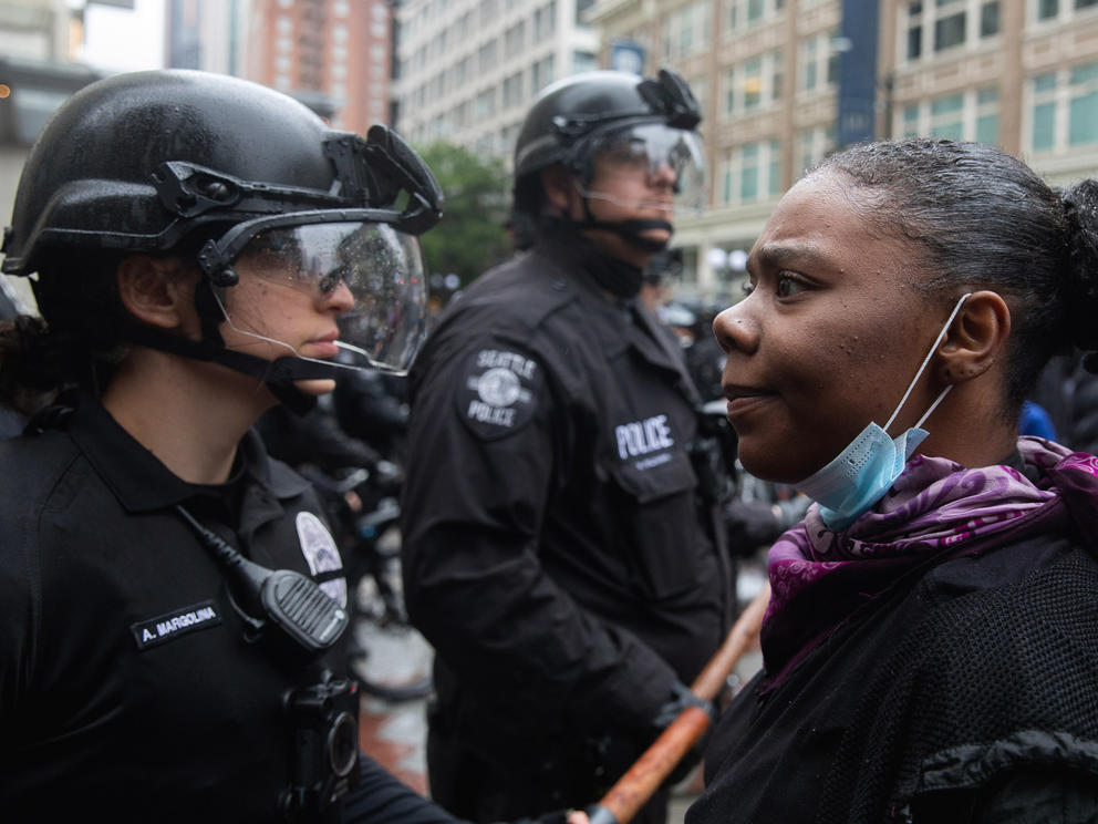 A helmeted bike officer at left stands face-to-face with a demonstrator