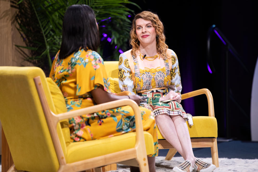 Two women sit in comfy chairs on stage, chatting