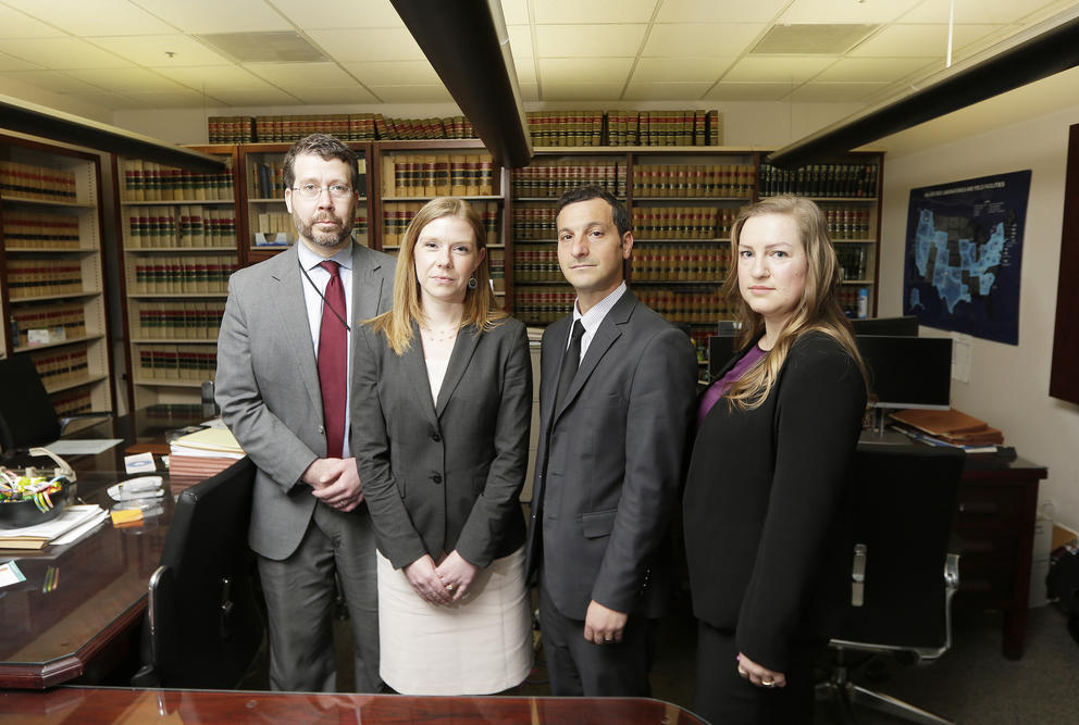 Four attorneys stand shoulder to shoulder in their legal office.