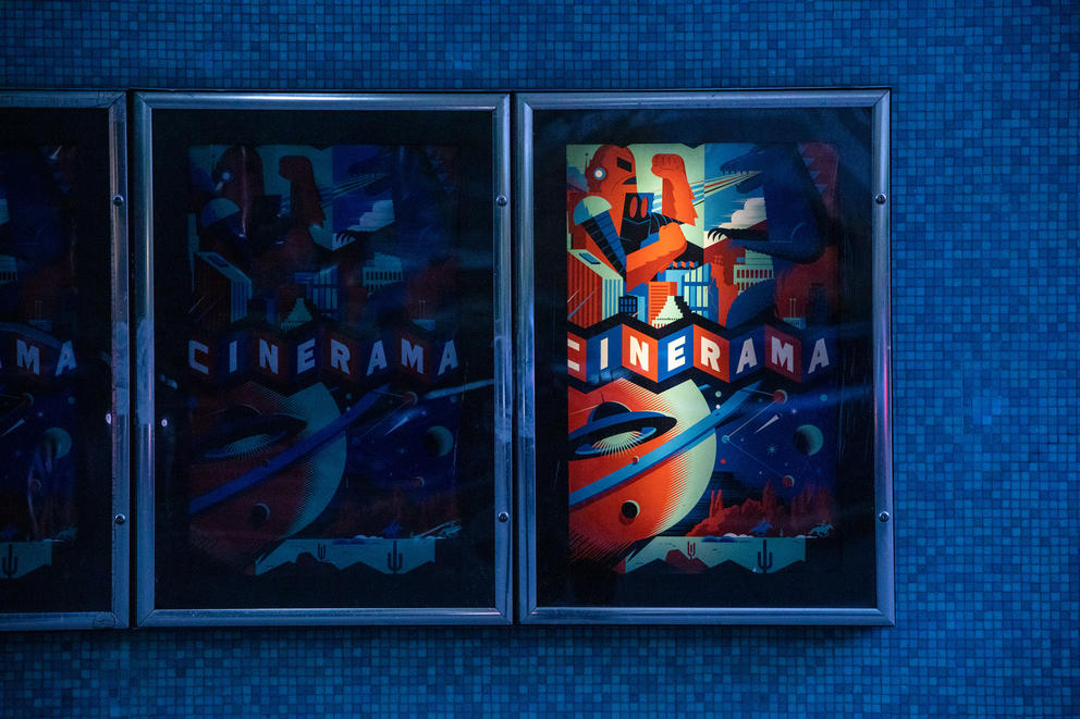 Movie posters against a blue wall, the one on the left is dark and the one on the right is light