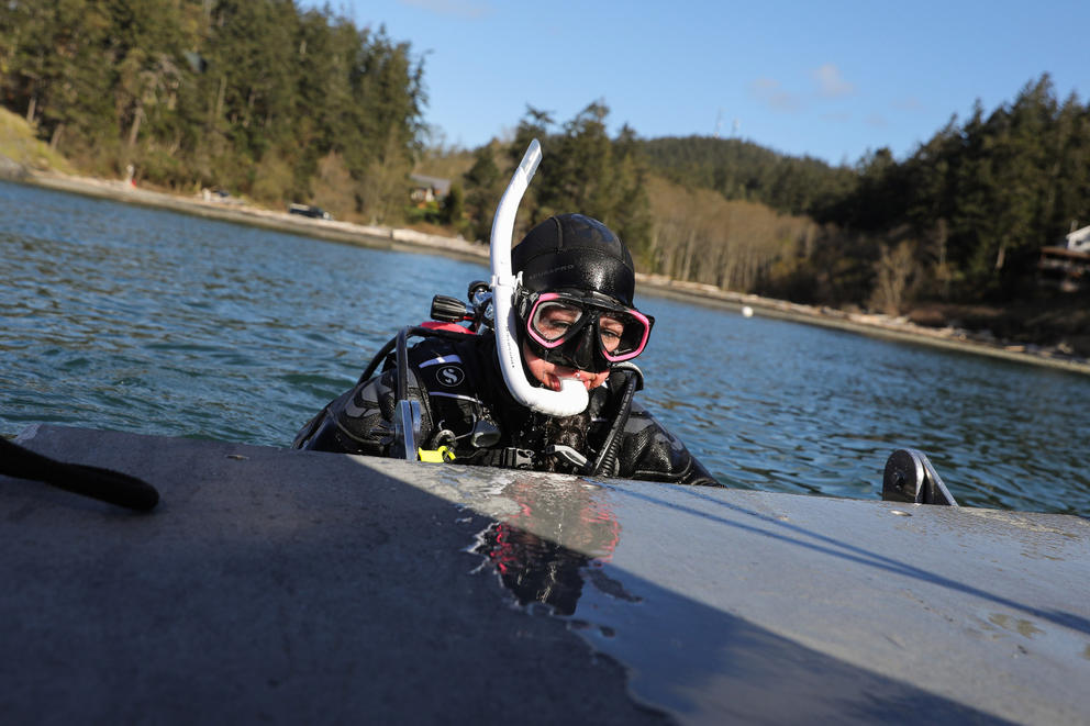 Jennie DeLaCruz, wearing diving gear, climbs out of the water and onto a boat