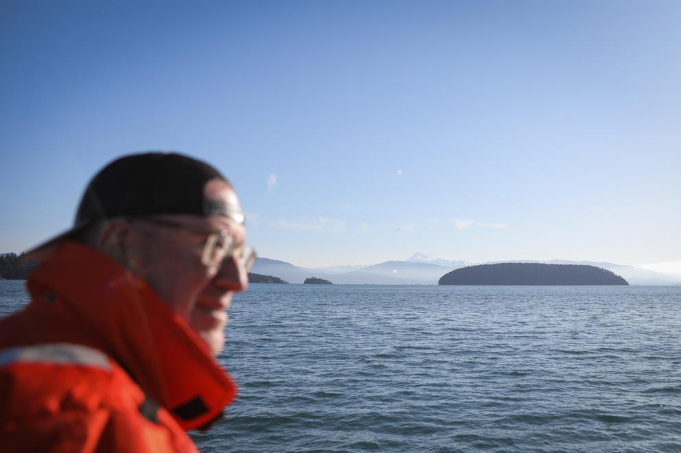 A man out of focus in the foreground looks out at the Salish Sea and San Juan Islands