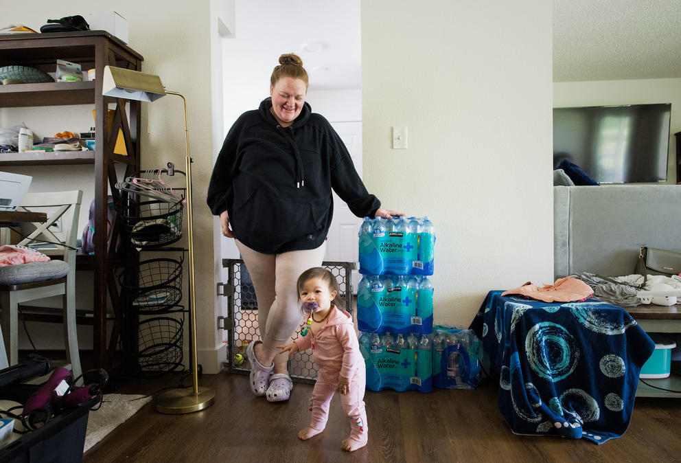 Heather Nguyen leans on cases of bottled water while watching her daughter Chloe in their home on the Joint Base Lewis-McChord base