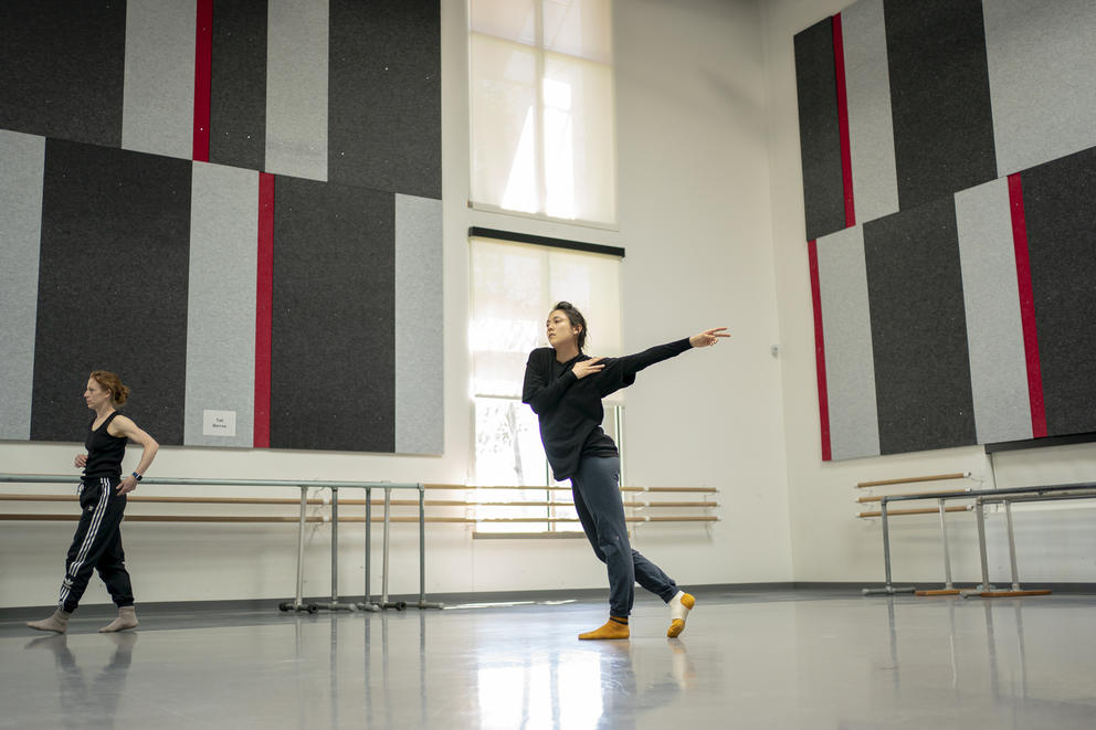 A wide shot of a dancer rehearsing in a studio, the choreographer walks out of the frame at the left