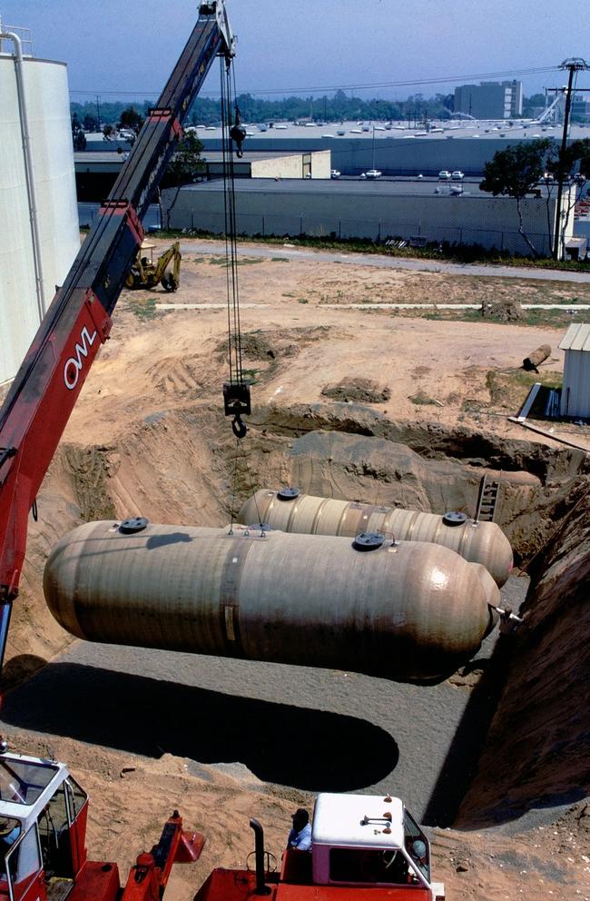 Double-walled, fiberglass storage tanks are prepared and lowered onto a gravel bed at a gas station site