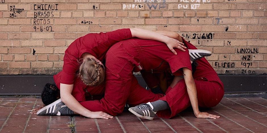 a group of dancers wearing red jumpsuits is tangled in a ball in front of a brick wall