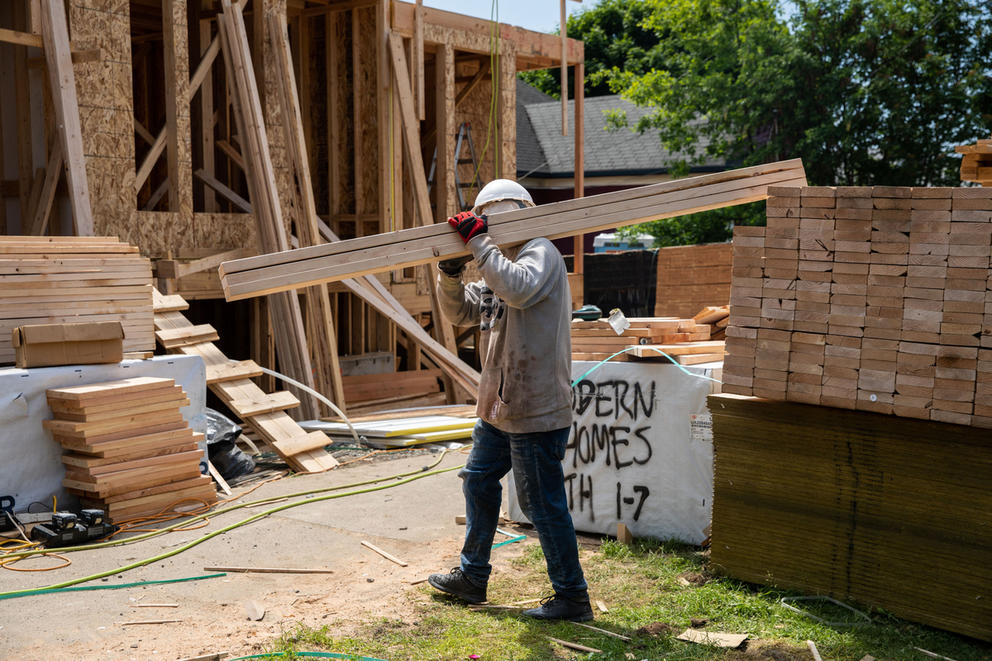 a construction worker carries a plank of wood on their shoulder