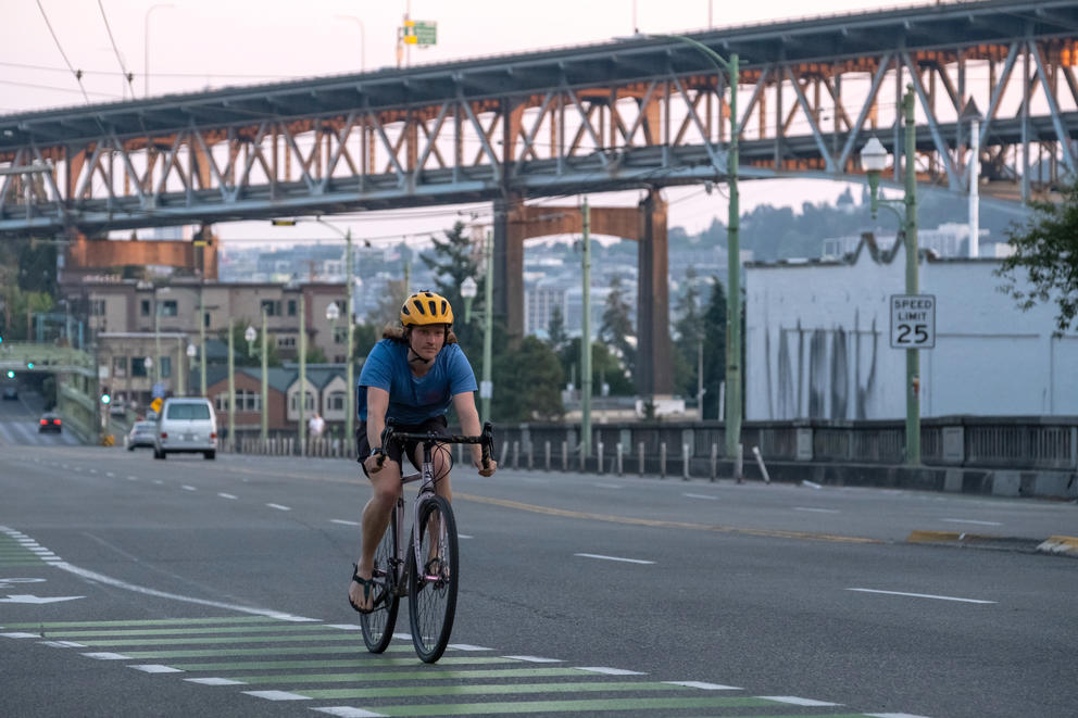 A man rides down a city street with a bridge behind