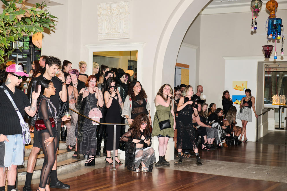 A crowd of people watch a runway fashion show and take pictures