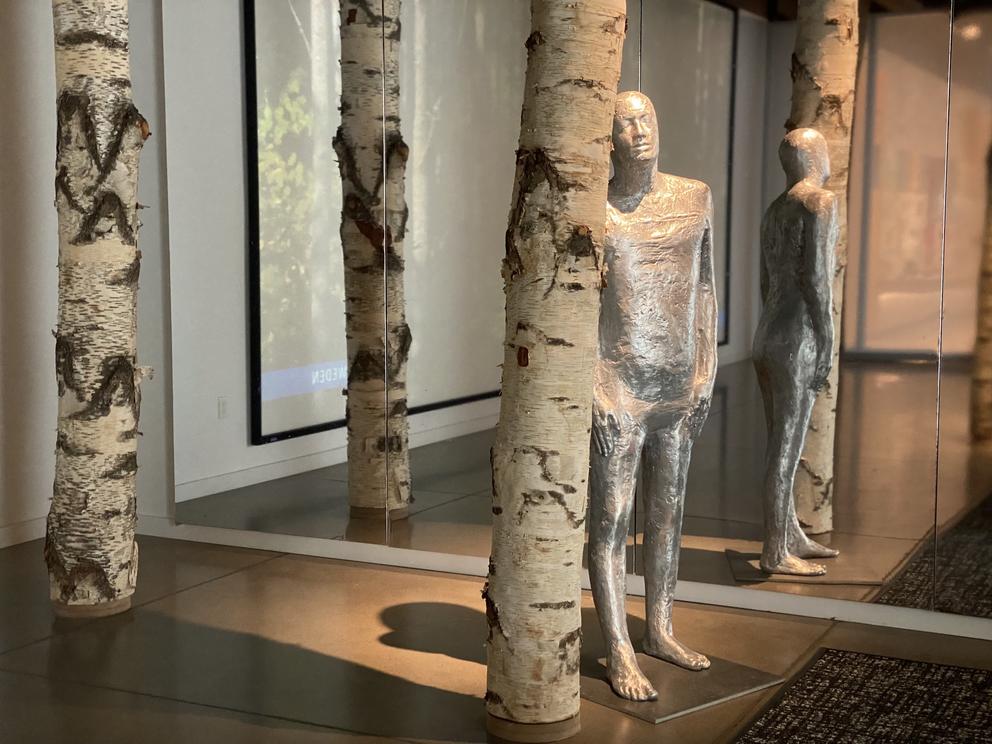 a gallery with a silver humanoid figure standing in a grove of birch trees
