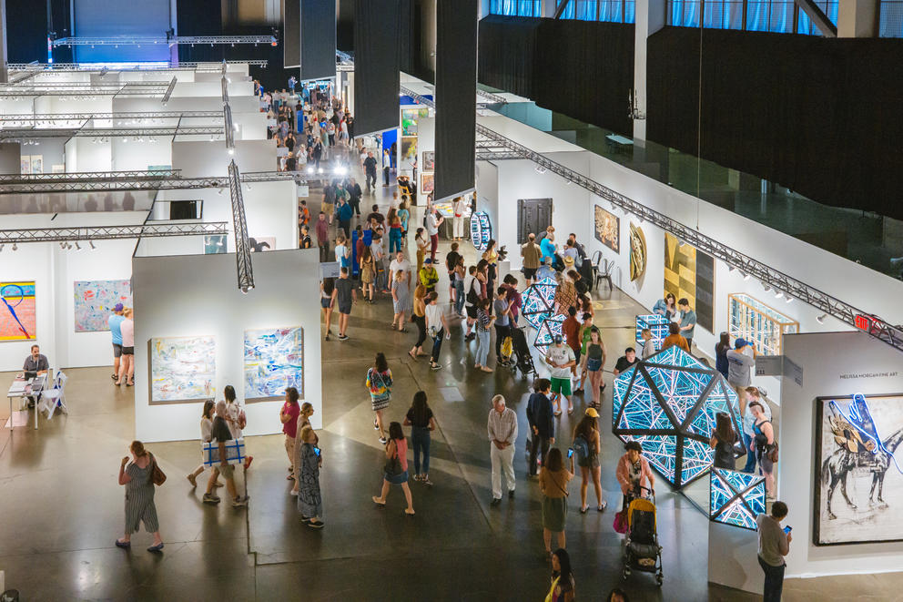 an overview photo of an art fair with many white cubes and people wandering through