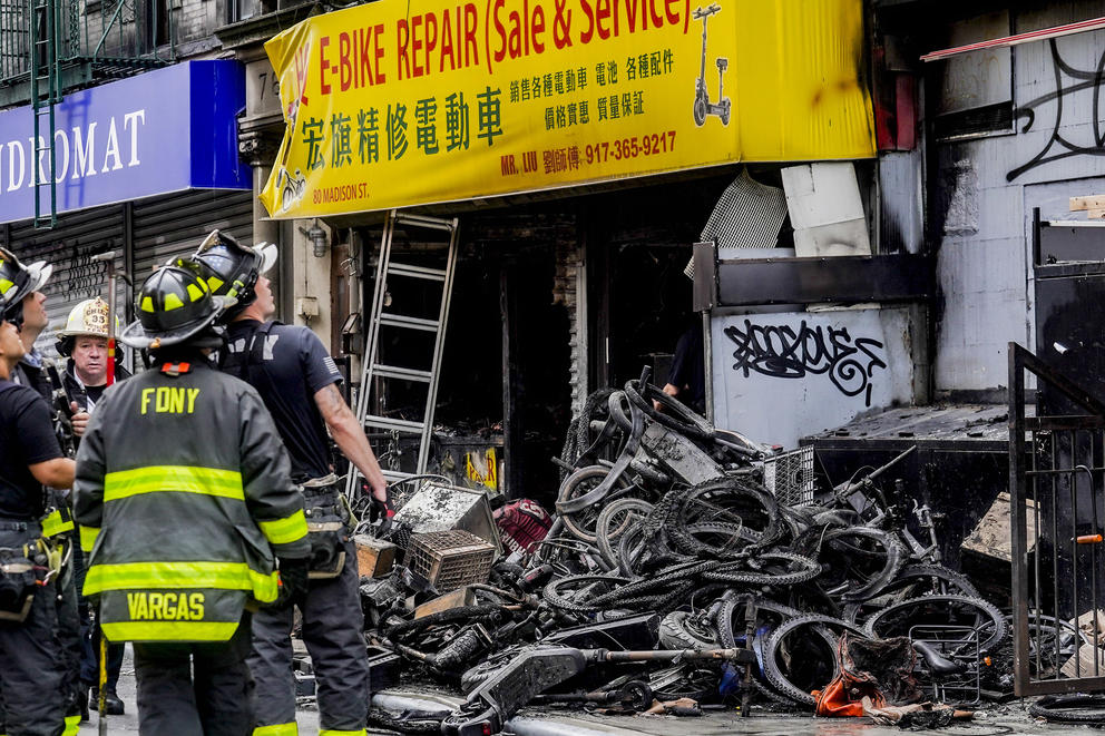 Firefighters in front of a the remains of an e-bike storefront.