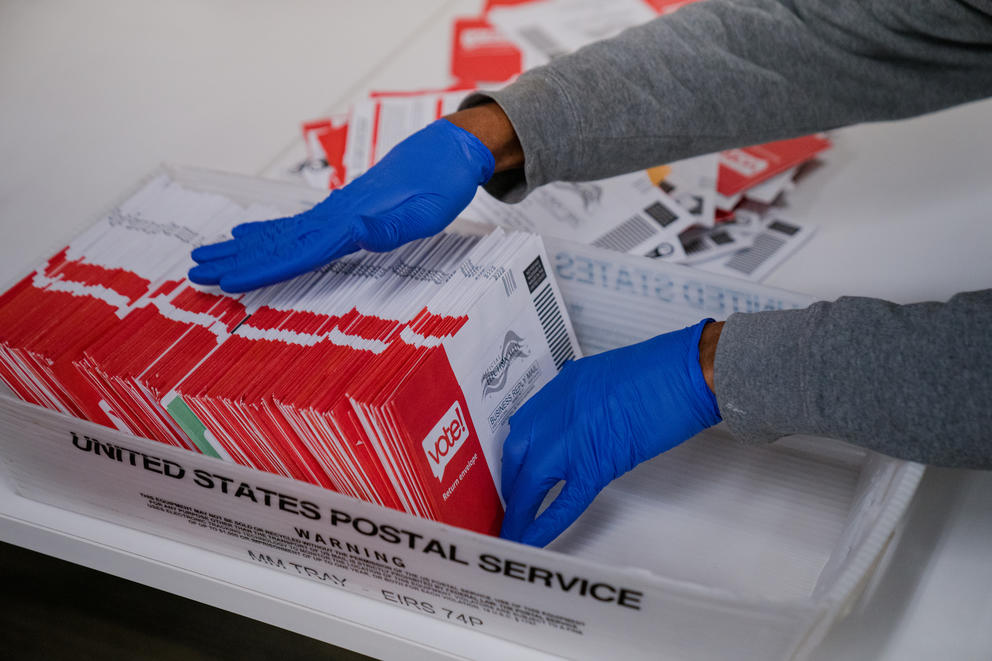 A picture of an election worker handling mail ballots.