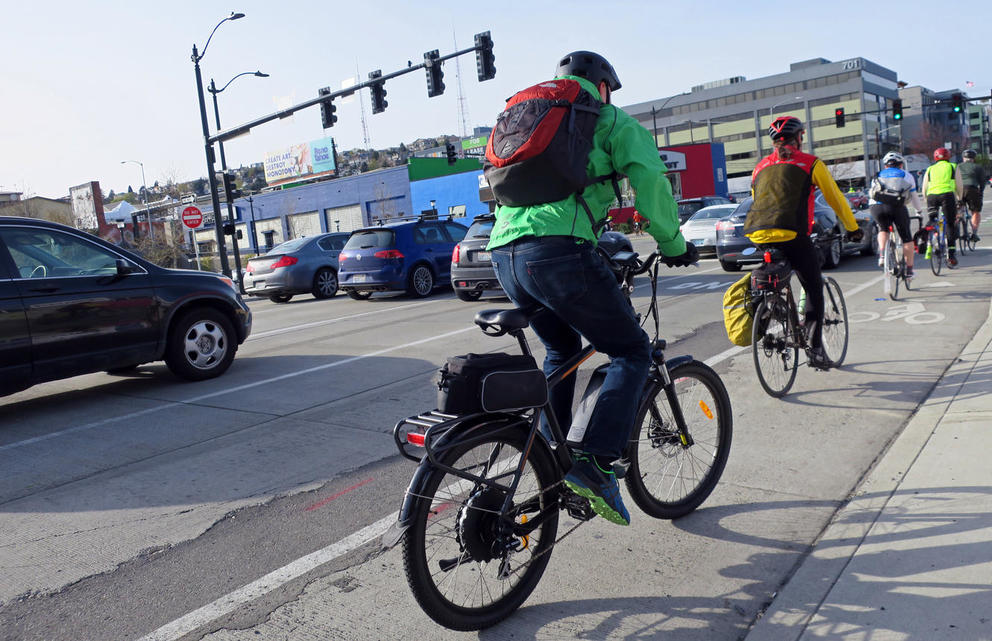 People ride e-bikes in a bike lane on a Seattle street.