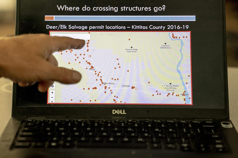A person points to a computer screen that displays a map with dots along a road.