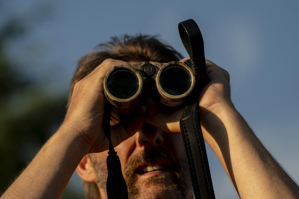A person peers through binoculars into the distance.