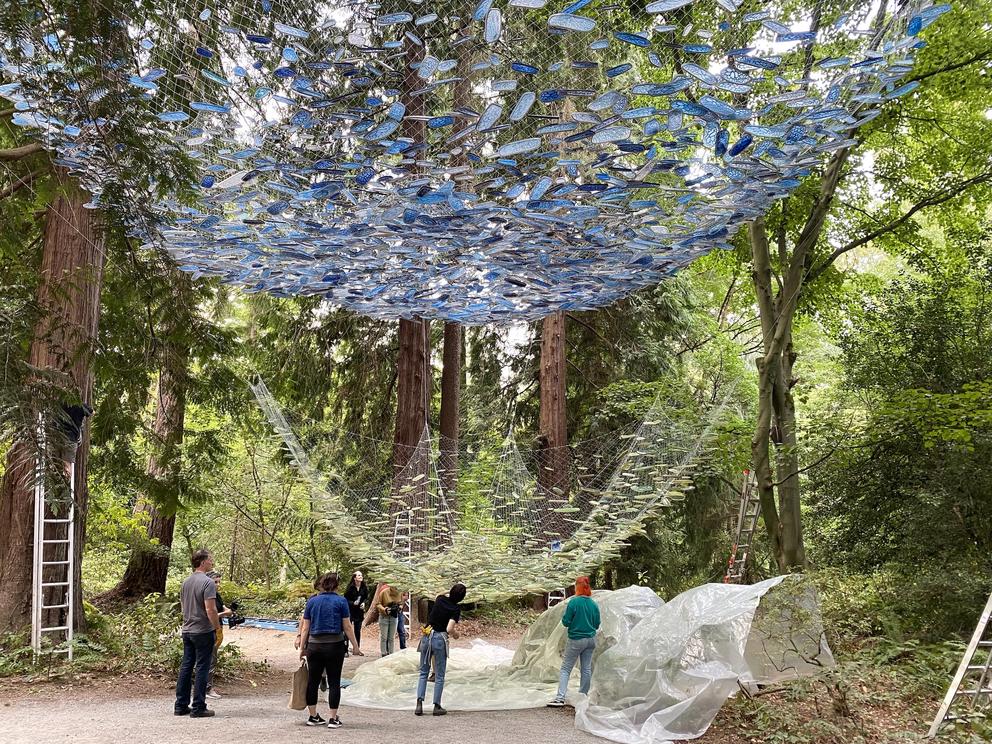 photo of an art installation in progress, with a net filled with green resin pieces is being raised up