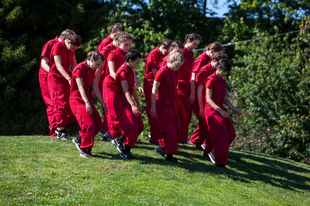 photo of a group of dancers on a grassy green hillside, all wearing red jumpsuits