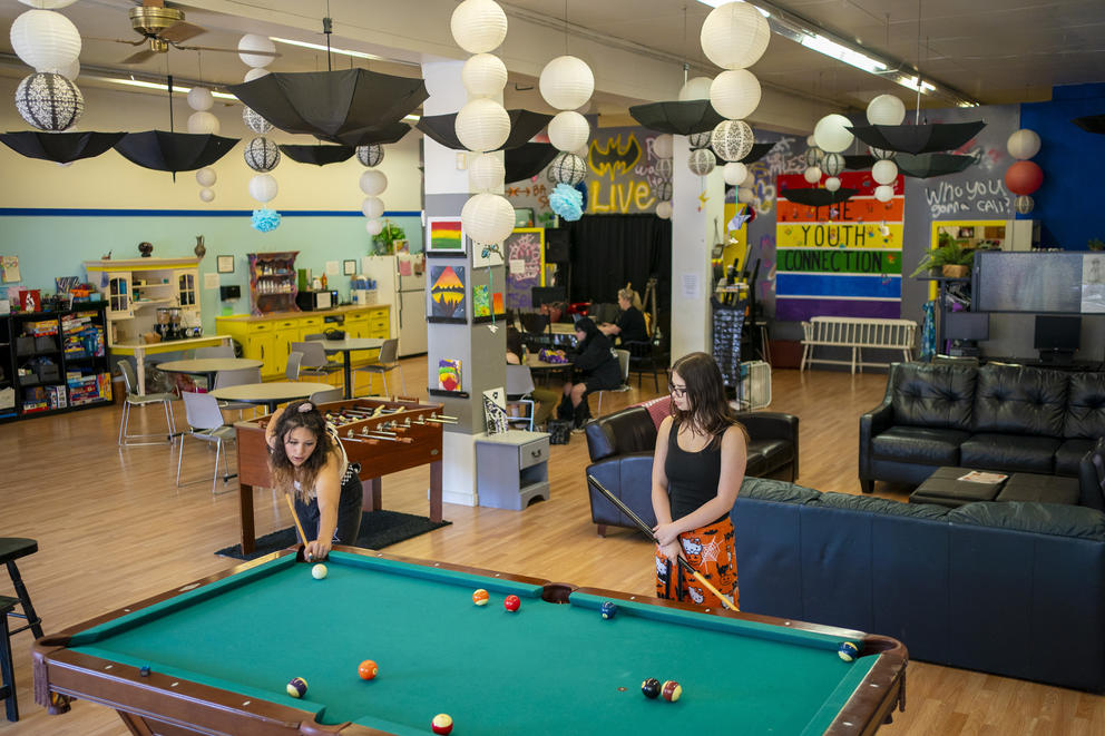 Two teens play pool in a brightly decorated lounge area at The Youth Connection.