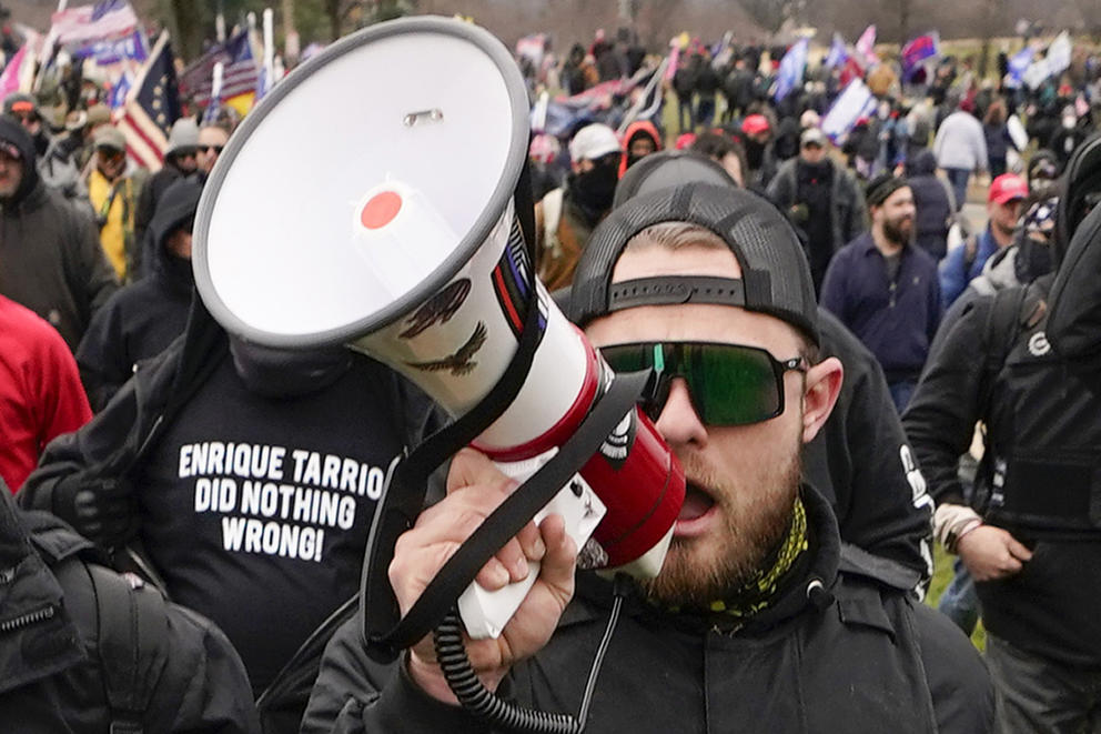 A man in a backwards hat speaks into a megaphone amidst a crowd