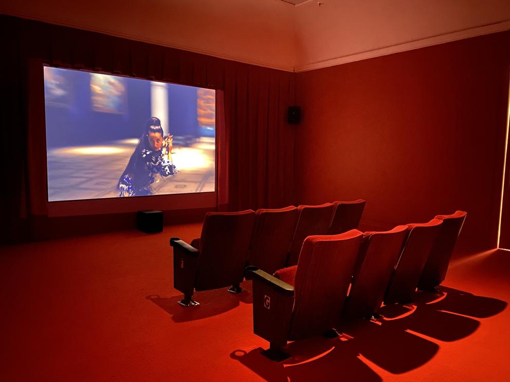 photo of a red-lit movie screening room with a woman wielding a sword on screen