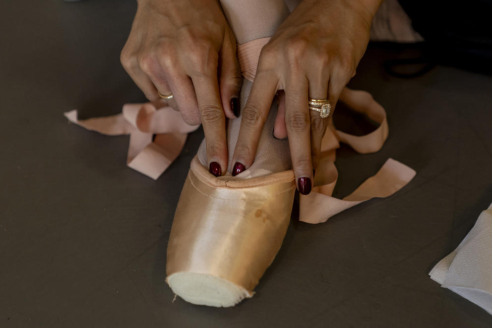 A close-up image of someone putting on pointe shoes