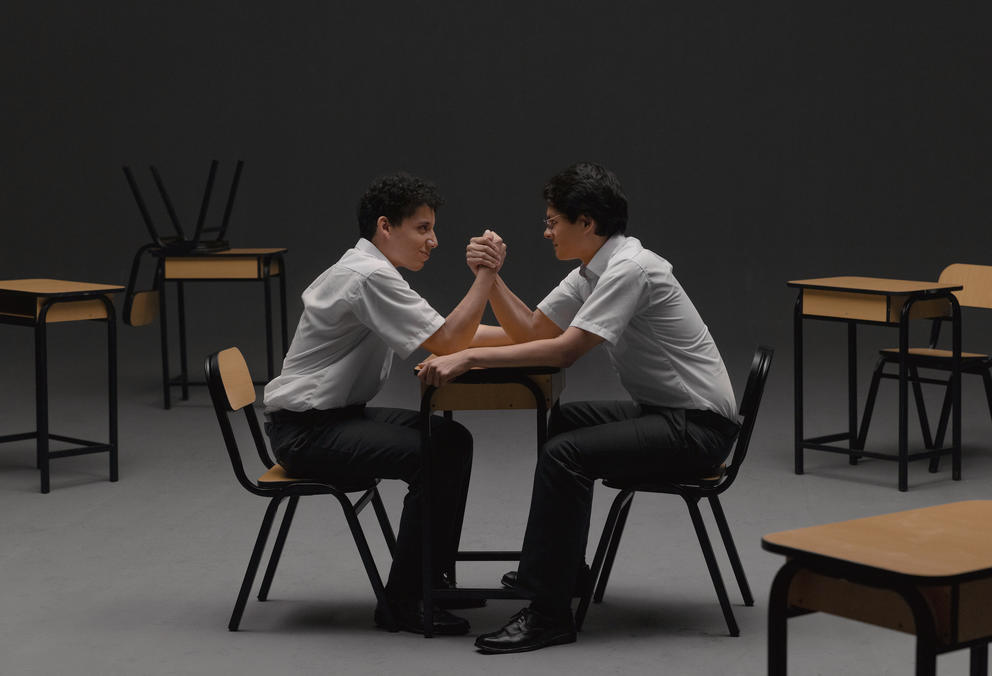 photo of two teen boys arm wrestling across a school desk