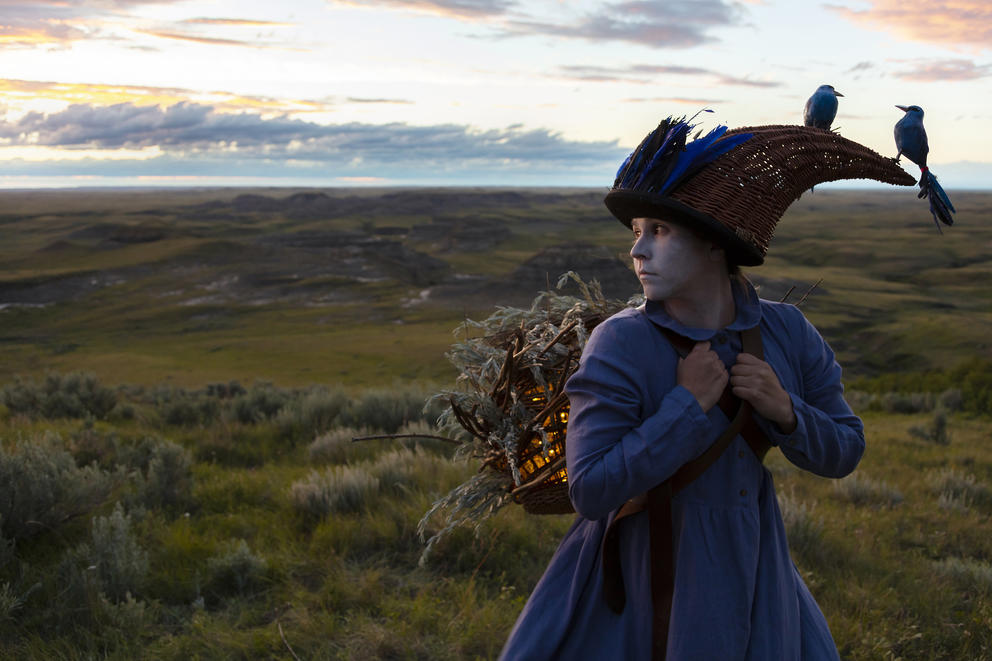 photo of a woman wearing a cornucopia-like hat with birds on it amid a barren landscape 