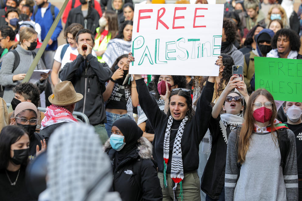 A woman in a crowd holds up a sign that reads "Free Palestine"