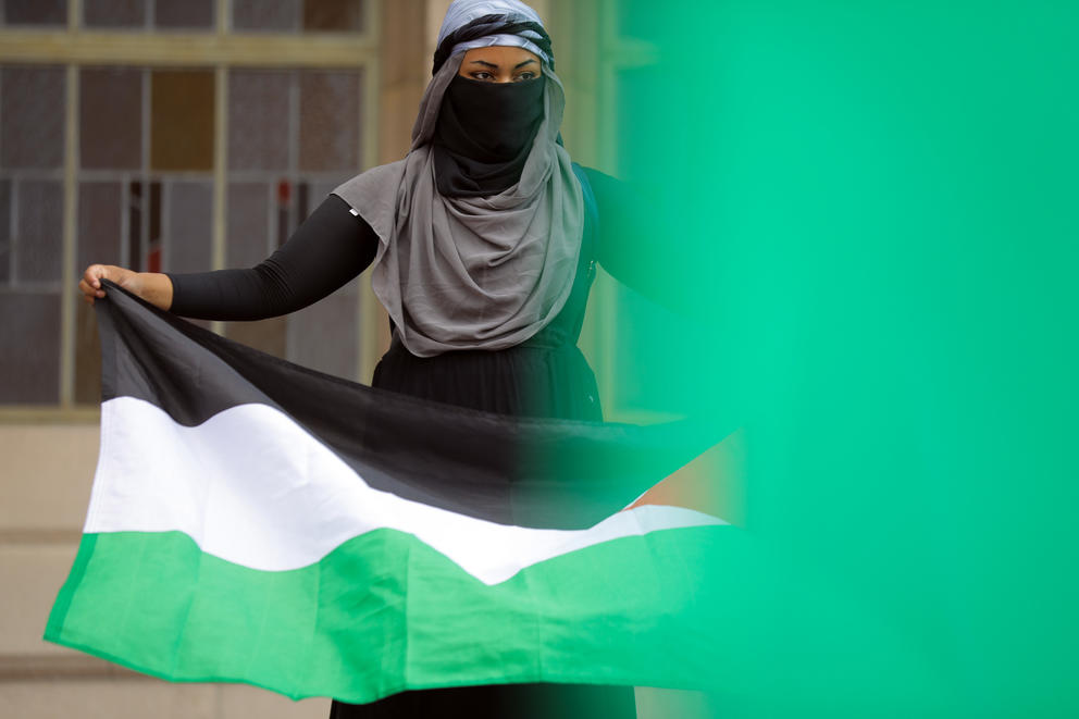 A woman with her face and head covered holds a Palestinian flag