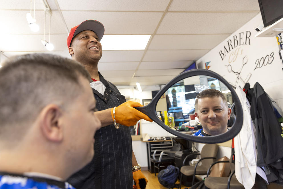 A man views his haircut in a hand mirror held by his barber.
