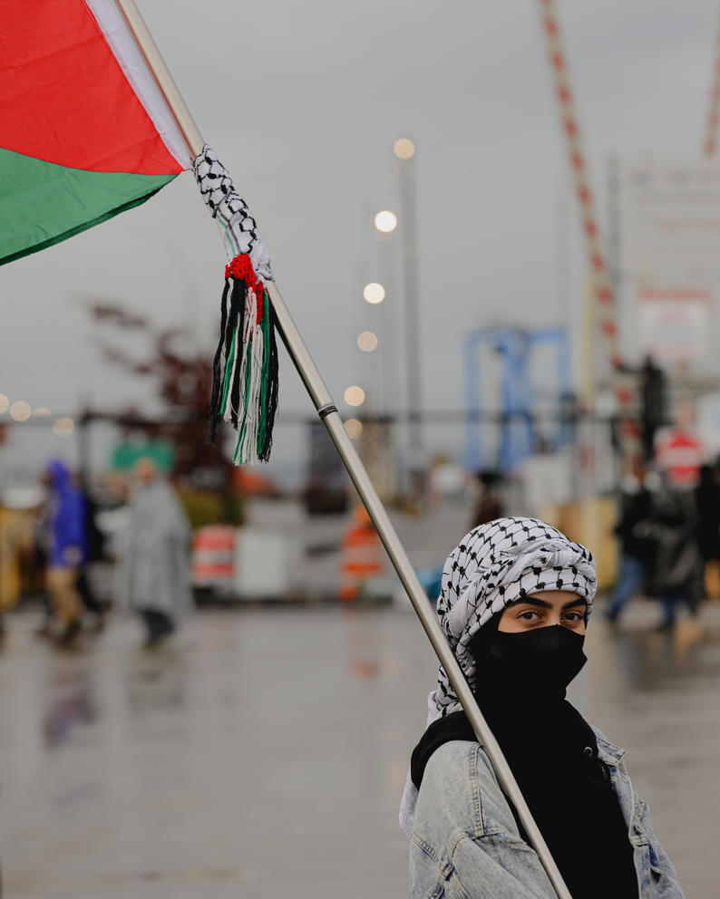 A protester holds a Palestinian flag as the march in front of the entrance to the Port of Tacoma