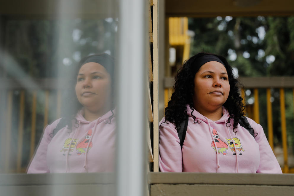 Janell Braxton sits reflected against a window in a pink sweatshirt