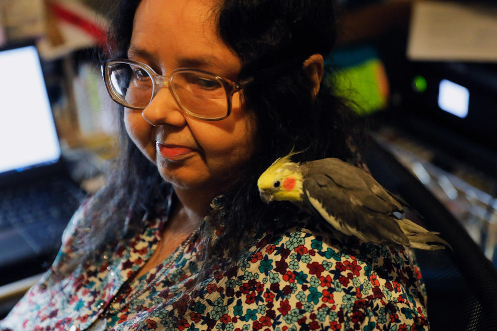 Debra Braxton sits in a floral shirt with a small, yellow-headed bird perched on her shoulder