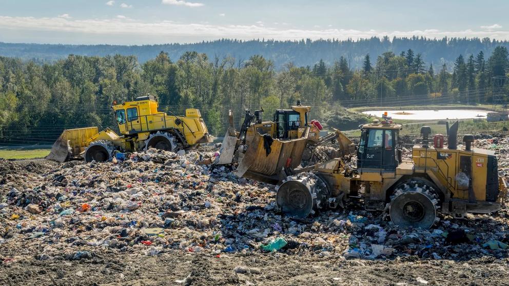 Three bulldozers move trash around a landfill.