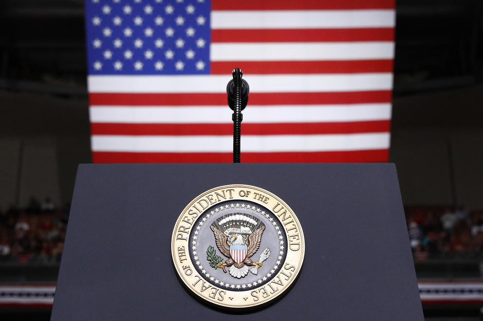 A podium with a President of the United States seal is pictured in front of an American flag 