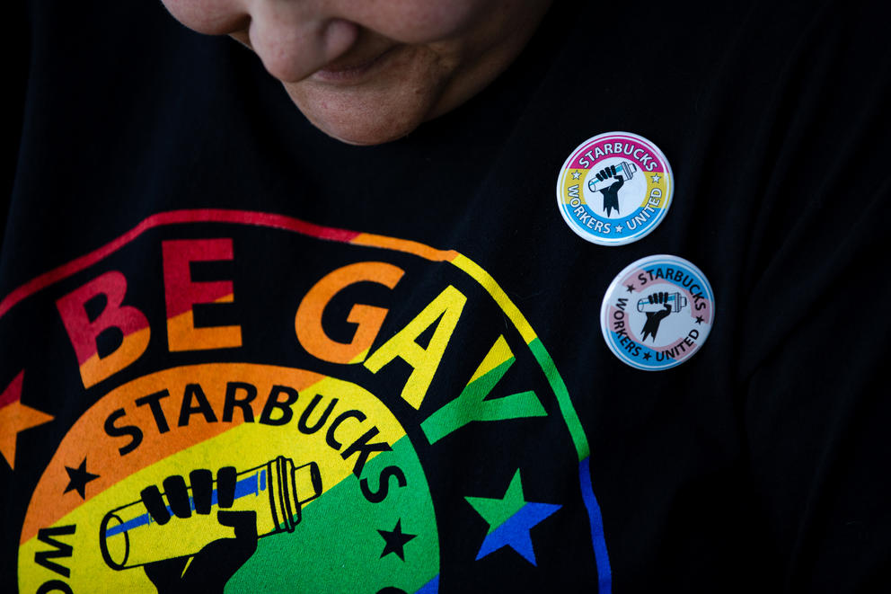 A Starbucks worker wears a rainbow union shirt with pins supporting unionization