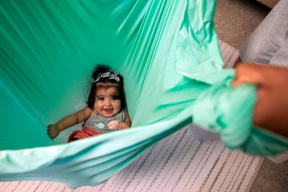 A baby smiles up from being held in a green sheet