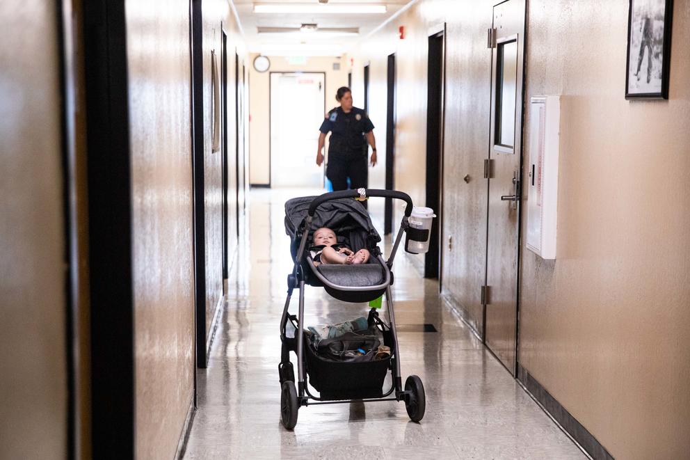 A baby in a stroller in the hallway of the prison, a guard is out of focus in the background