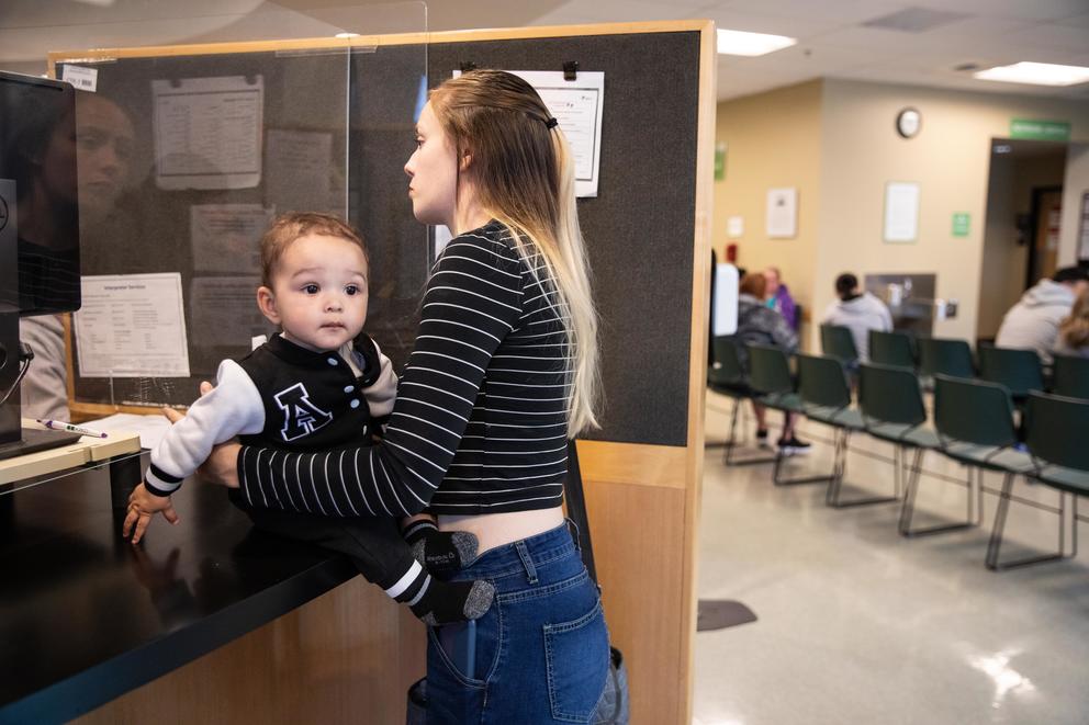 Paige Zorn holds her baby on the counter in an office as she speaks to an employee of the Department of Social and Health Services
