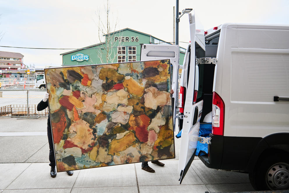 Two people move a large painting into the back of a van