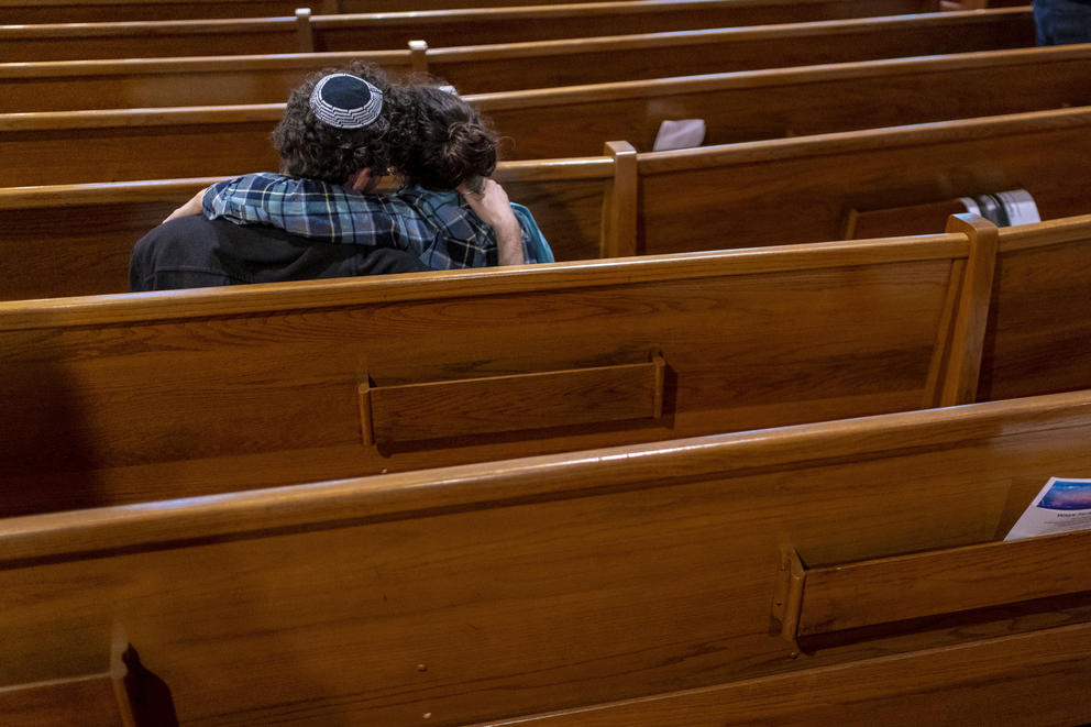 Two people are seen from behind huddle together in the pews of a synagogue
