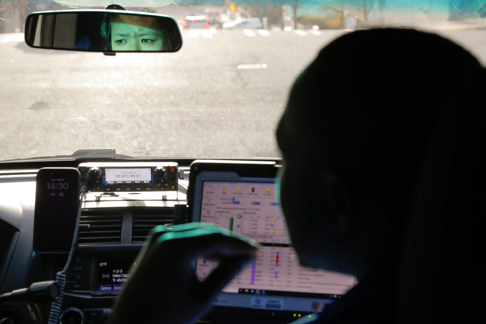 A woman's eyes are seen in a rearview mirror next to a silhouette of a man's head in a car. 