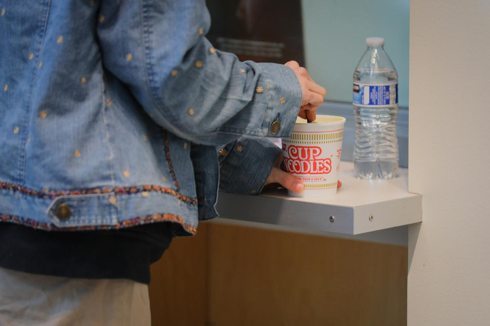 A close up of a woman's arm and hand as she stirs a cup noodle with a fork