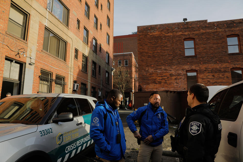 Two CARE team members stand with a Seattle Police officer between two cars and buildings