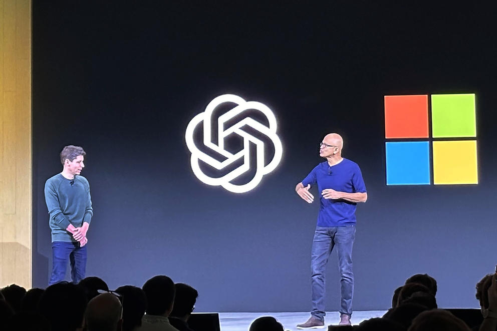 Two people are on a stage in front of a screen displaying the OpenAI and Microsoft logos.