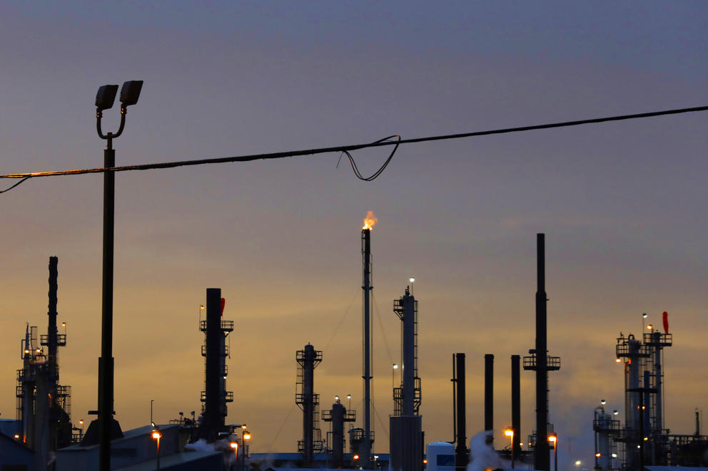 Stacks of an oil refinery are silhouetted at sunset