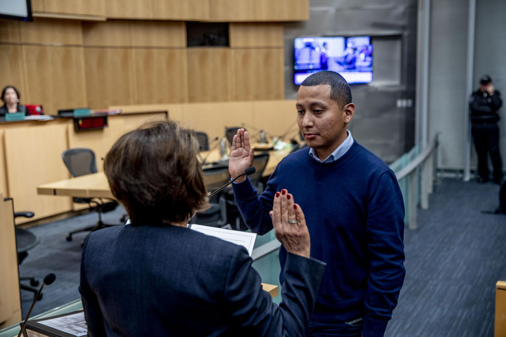 a man holds his right hand up to be sworn into the seattle city council