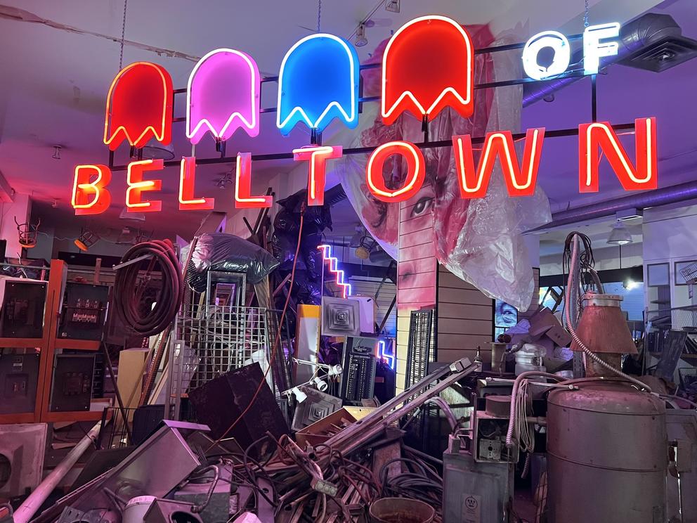 photo of a storefront with lots of junk piled inside and a neon sign with ghost figures